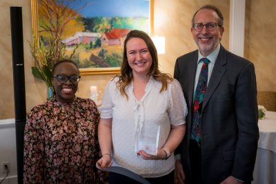 Three people, woman in center holding an award